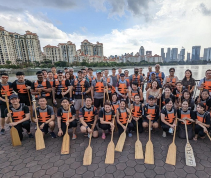 Grupo de funcionários com coletes salva-vidas segurando remos de barco em frente a um lago